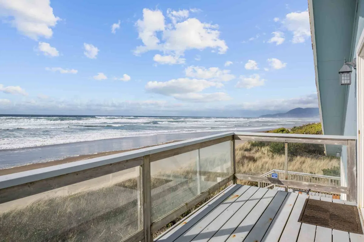 A tranquil perspective from a balcony overlooking gentle ocean waves and a stretch of sandy beach. The scene includes a balcony railing in the foreground, creating an inviting place to relax and take in the coastal environment.