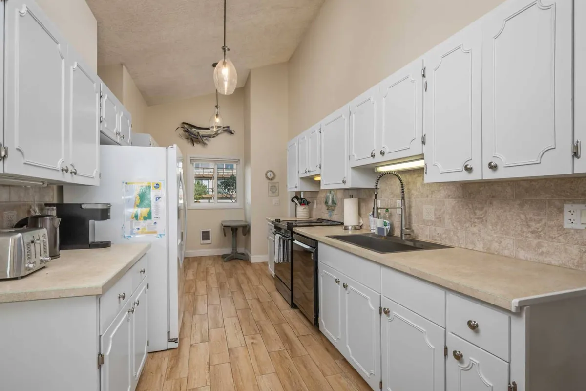 A modern, secondary kitchen highlighted by sleek white cabinetry, stainless steel appliances, and a window with a scenic view. The space is designed for culinary flexibility and is ideal for group meal prep or accommodating multiple families.