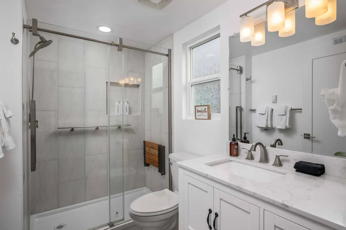 A modern bathroom featuring a glass shower enclosure, a marble countertop, contemporary light fixtures, and subtle beach-themed decor. The space feels fresh, calming, and inviting—ideal for self-care and relaxation.