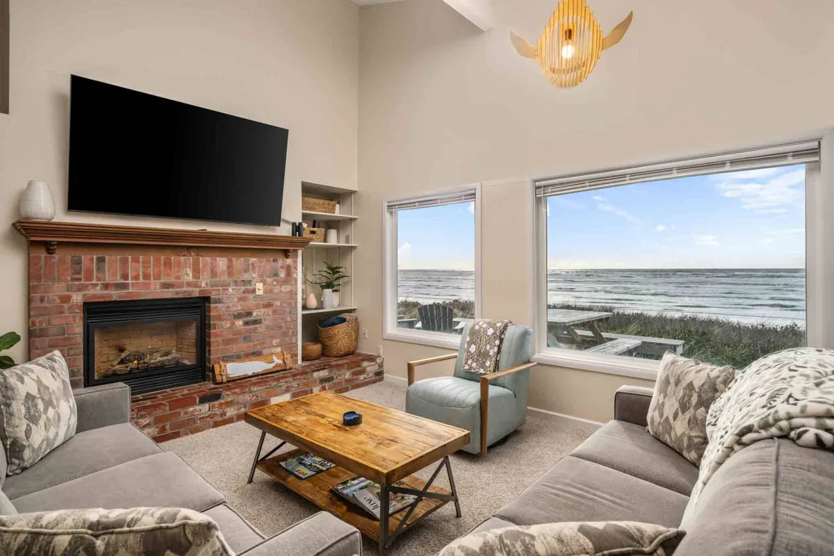 A cozy living space with comfortable seating, a wood coffee table, and a gas fireplace. Large windows frame breathtaking ocean vistas, filling the room with light and a tranquil ambiance perfect for relaxing after a shared meal or during a quiet evening.