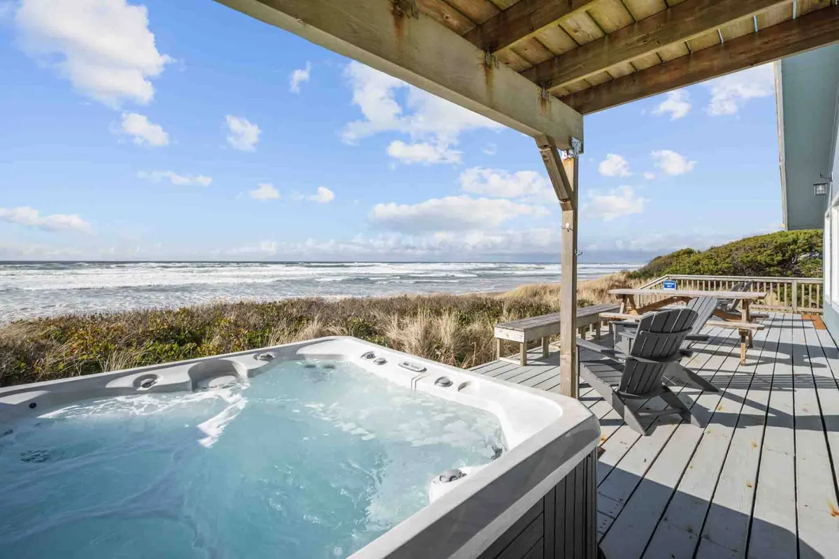 A serene deck area featuring a hot tub and a cozy seating arrangement, all overlooking the Pacific Ocean. The layout encourages socializing or peaceful solitude, with the hot tub offering front-row seats to sunset and ocean vistas.