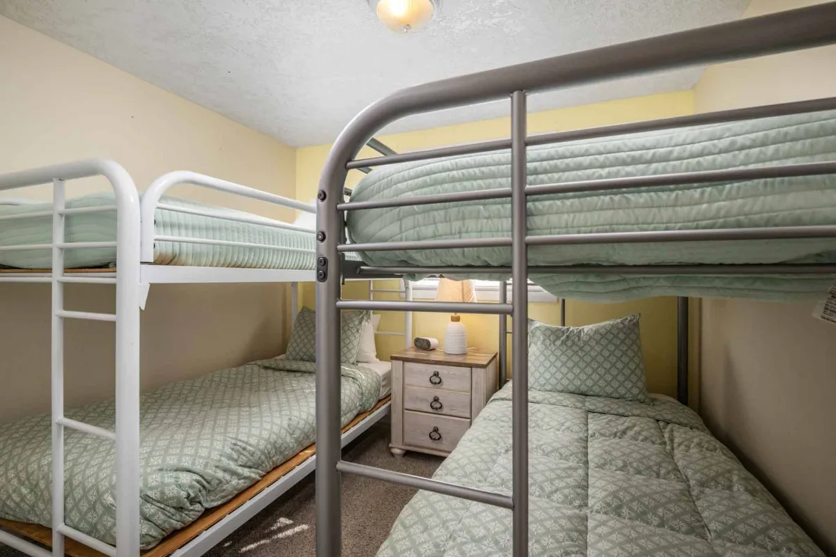 This image features a cozy bedroom with bunk beds, a nightstand, and a decorative pillow, evoking a welcoming and relaxed environment ideal for children or multiple guests. The setting clearly conveys kid-friendly sleeping arrangements and shared, joyful experiences.