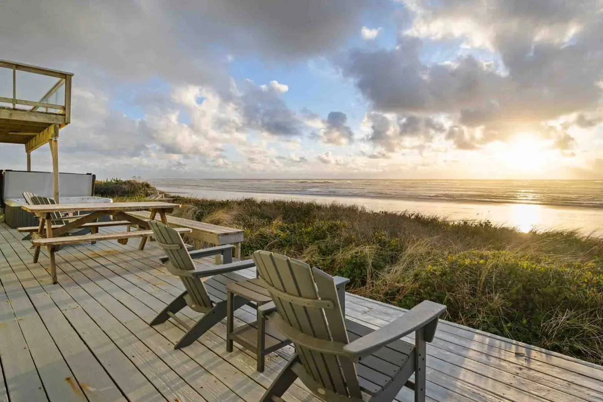 A serene sunset scene featuring a wooden deck with adirondack chairs facing the ocean, bathed in the warm glow of dusk. The view encourages moments of reflection and togetherness as day turns to night.