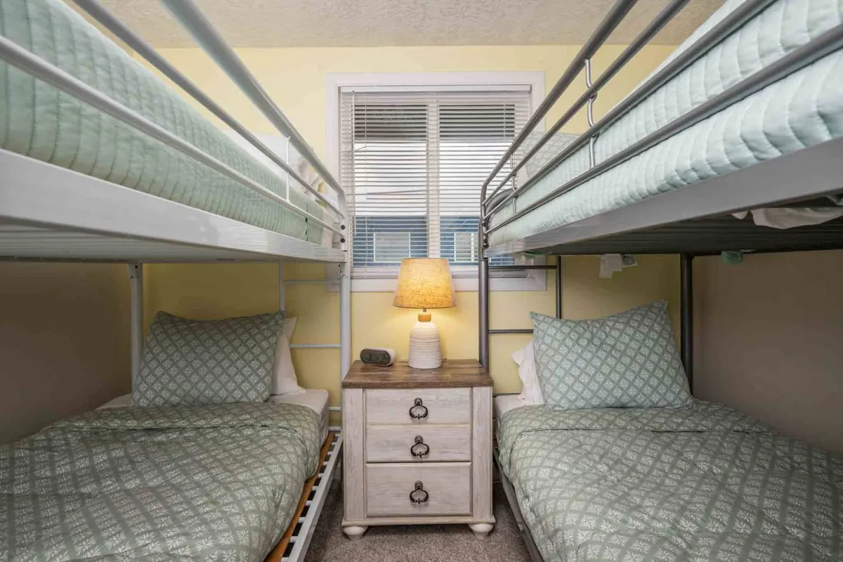 A cheerful bunk room with two sets of bunk beds, a nightstand with a lamp, and a bright window. The layout is inviting for kids or friends, with cozy bedding and a playful atmosphere that encourages late-night stories and bonding.