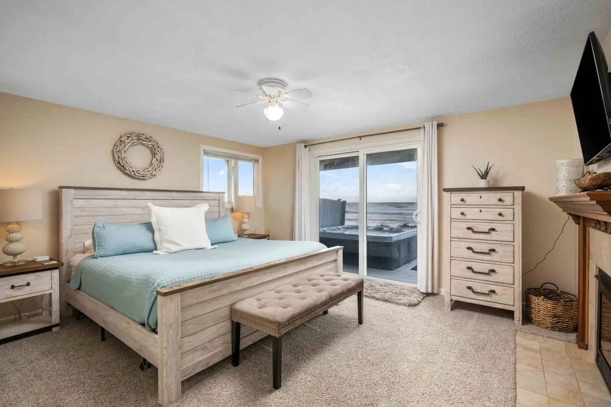 A serene bedroom featuring a plush bed with soft bedding, a sliding glass door that opens to an outdoor view, a dresser, and a nightstand. Natural light fills the space, and the room feels peaceful and welcoming—ideal for moments of relaxation.
