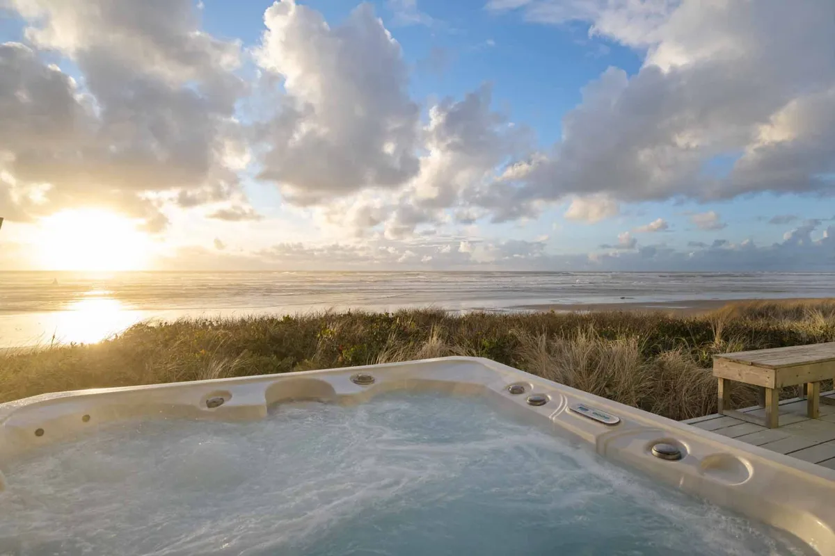 A stunning sunset scene with a hot tub and unobstructed ocean views. The sky is ablaze with colors, and the warmth of the hot tub creates a comforting contrast to the cool ocean air, inviting guests to linger into the evening.