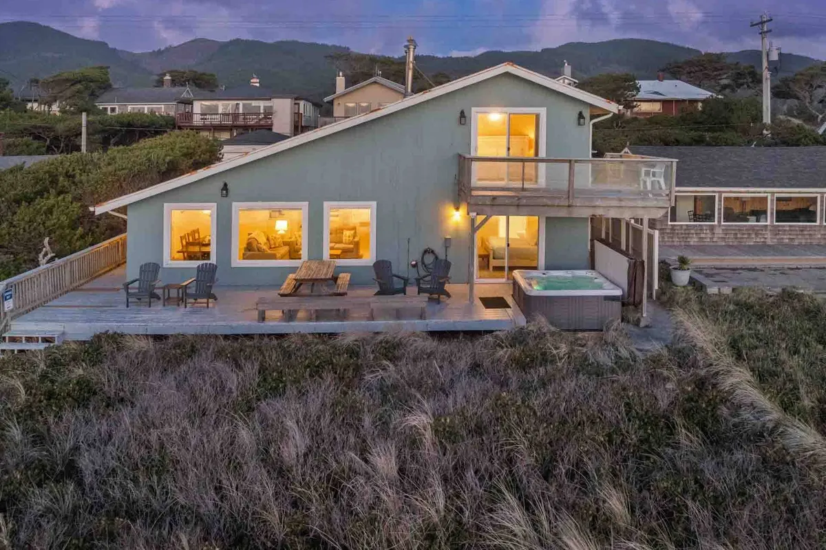 This image showcases an inviting deck area with ample seating, large windows that frame the ocean view, and a prominent hot tub. The warm, serene atmosphere is perfect for relaxing at sunset or gathering with friends and family outdoors. The hot tub is positioned to maximize enjoyment of both the view and the fresh ocean breeze.